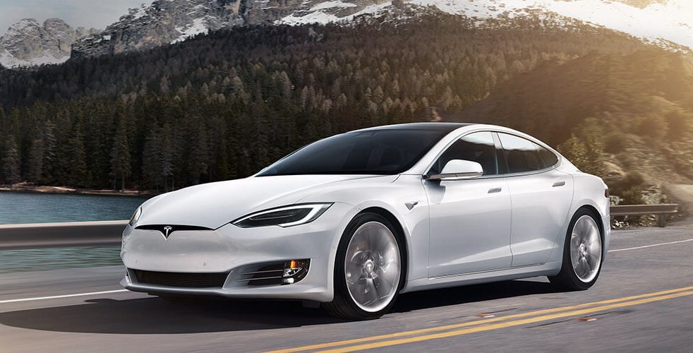 A white tesla model s is driving down the street.