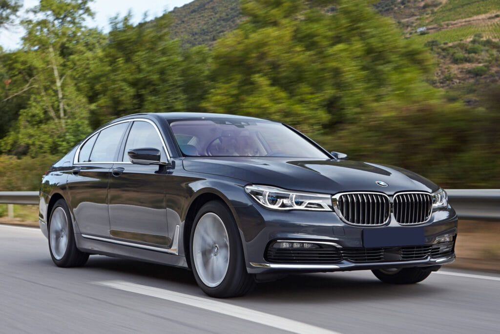 A bmw 7 series driving down the road near some trees.