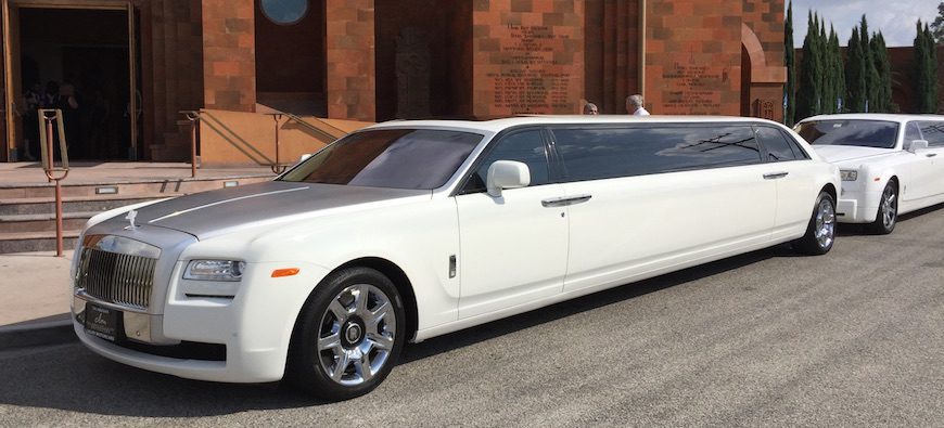 A white limo is parked in front of a brick building.