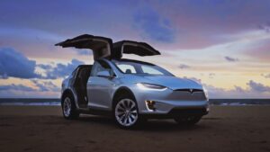 A silver tesla model x is parked on the road.