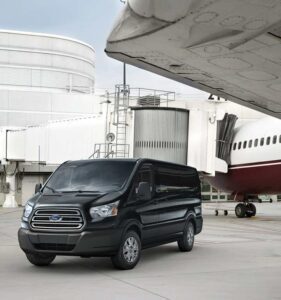 A black van parked in front of an airplane.