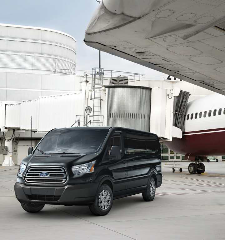 A black van parked in front of an airplane.