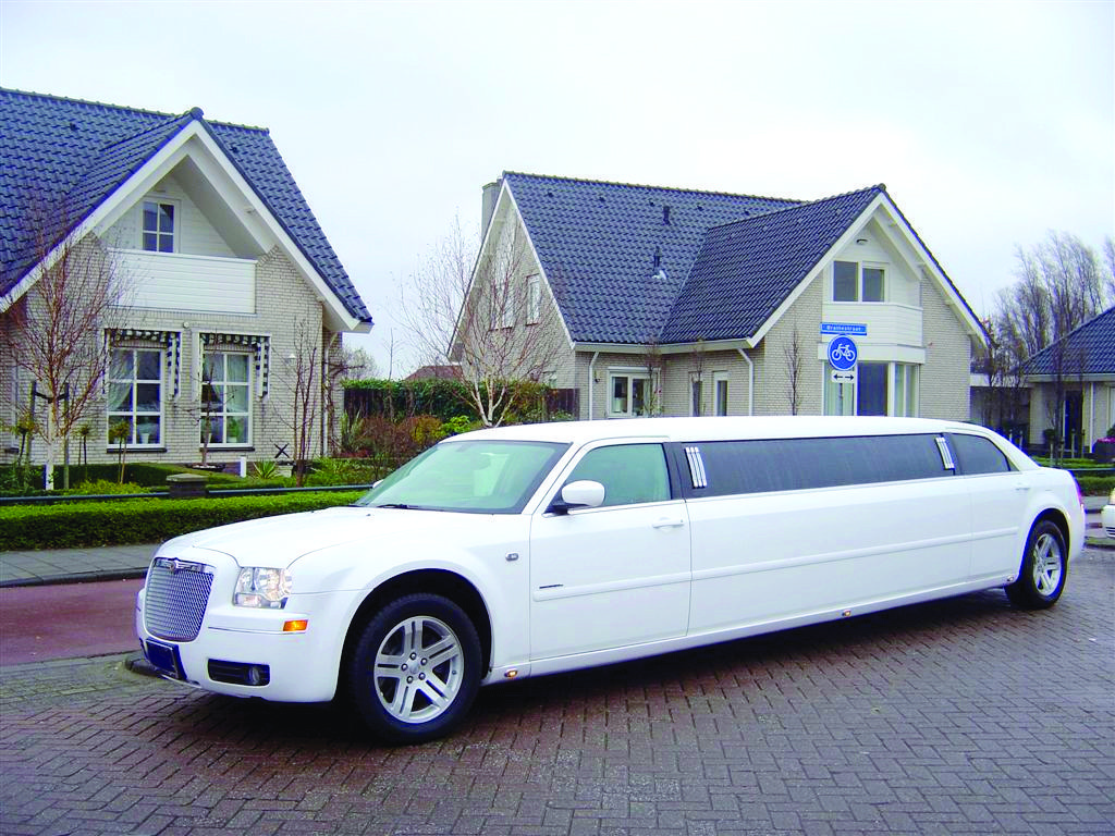 A white limo parked in front of two houses.