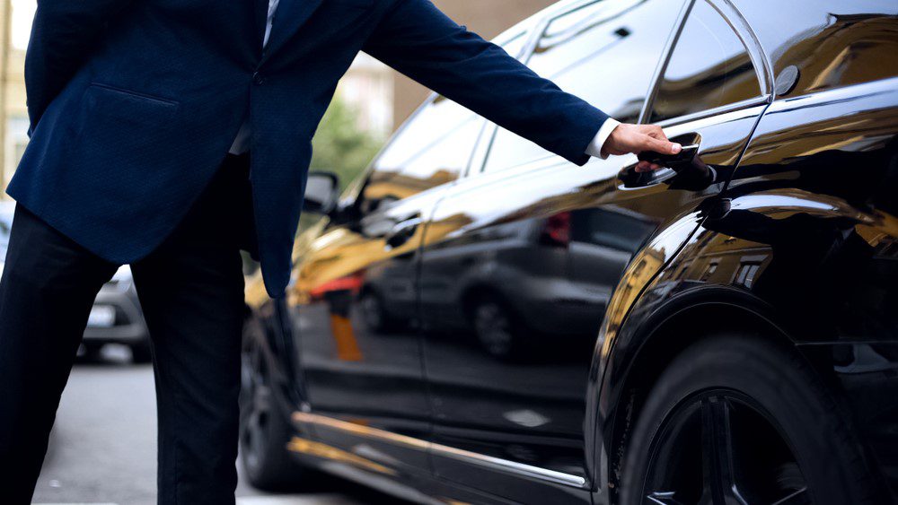 A man in a suit and tie standing next to a car.