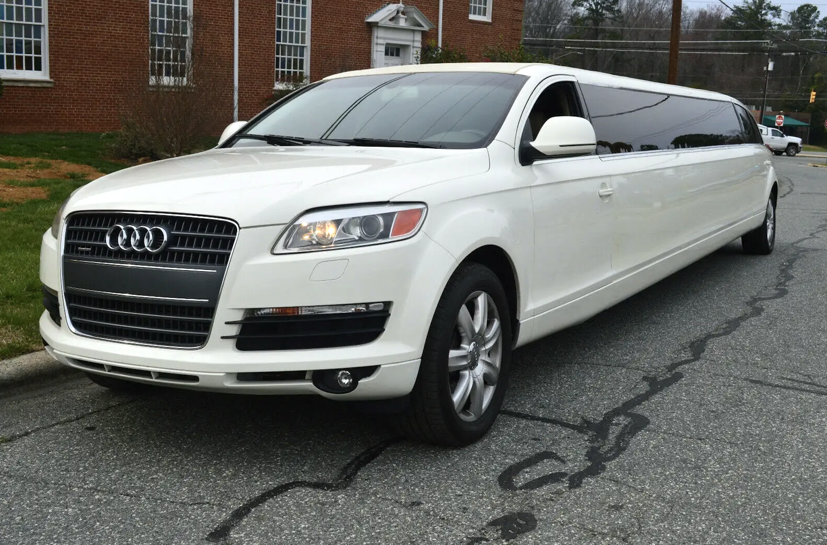 A white limo is parked in front of a brick building.