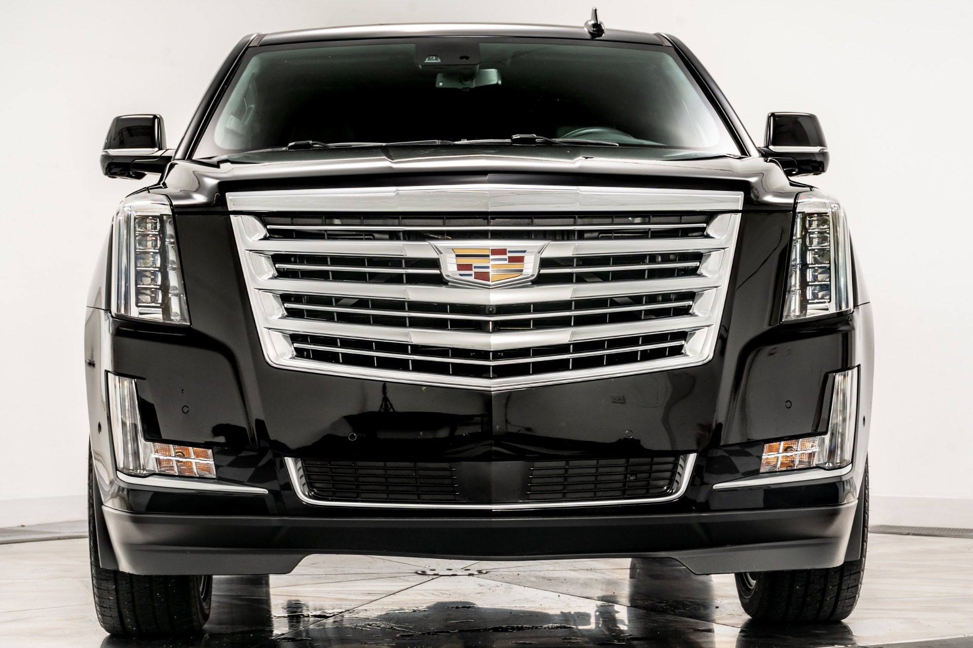 A black cadillac escalade is parked in front of a white wall.