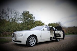 A white rolls royce parked on the side of a road.