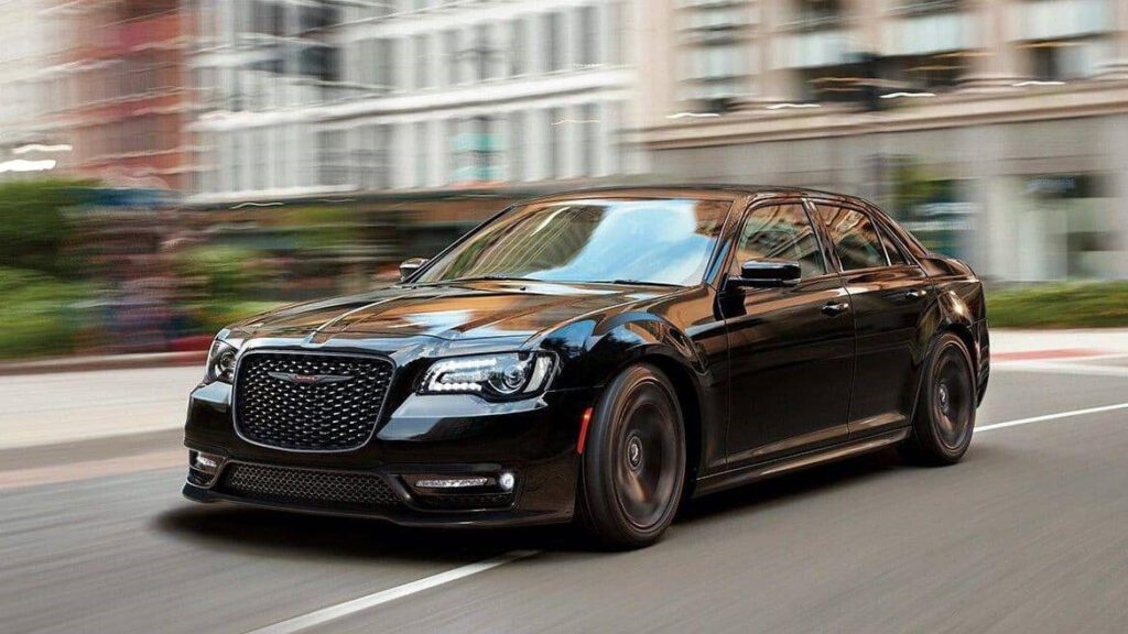 A black car driving down the street in front of some buildings.