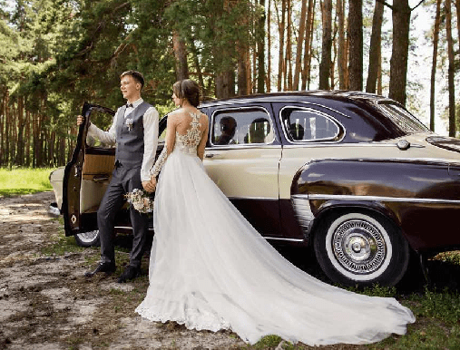 A man and woman standing next to an old car.