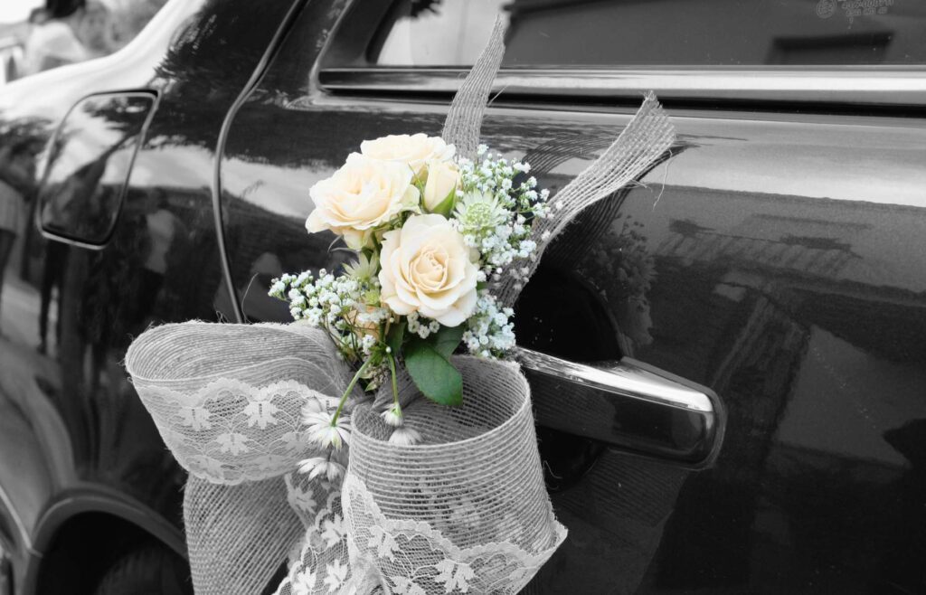 A bouquet of flowers is tied to the side of a car.