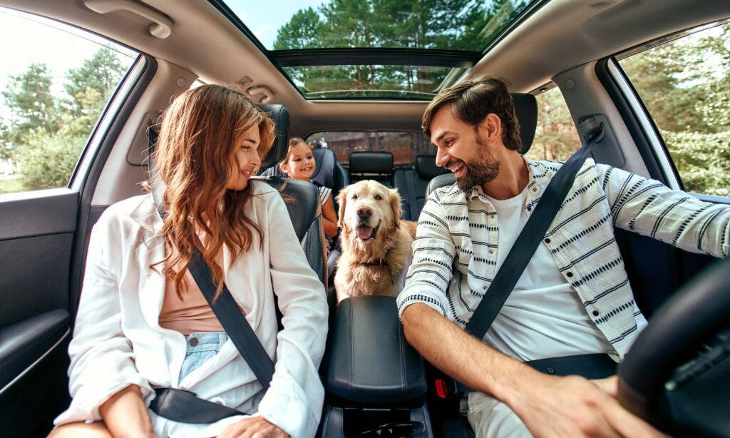 A man and woman in the back of a car with their dog.