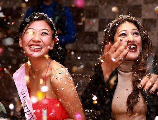 Two women are smiling and throwing confetti in the air.