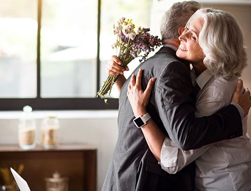 A man and woman hugging each other holding flowers.