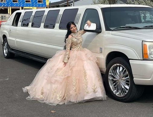 A woman in a long dress leaning on the side of a limo.